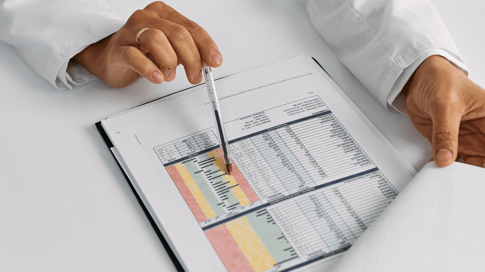 A clinician's hands review a printed report with a pen, suggesting a close look at air ambulance contract costs.