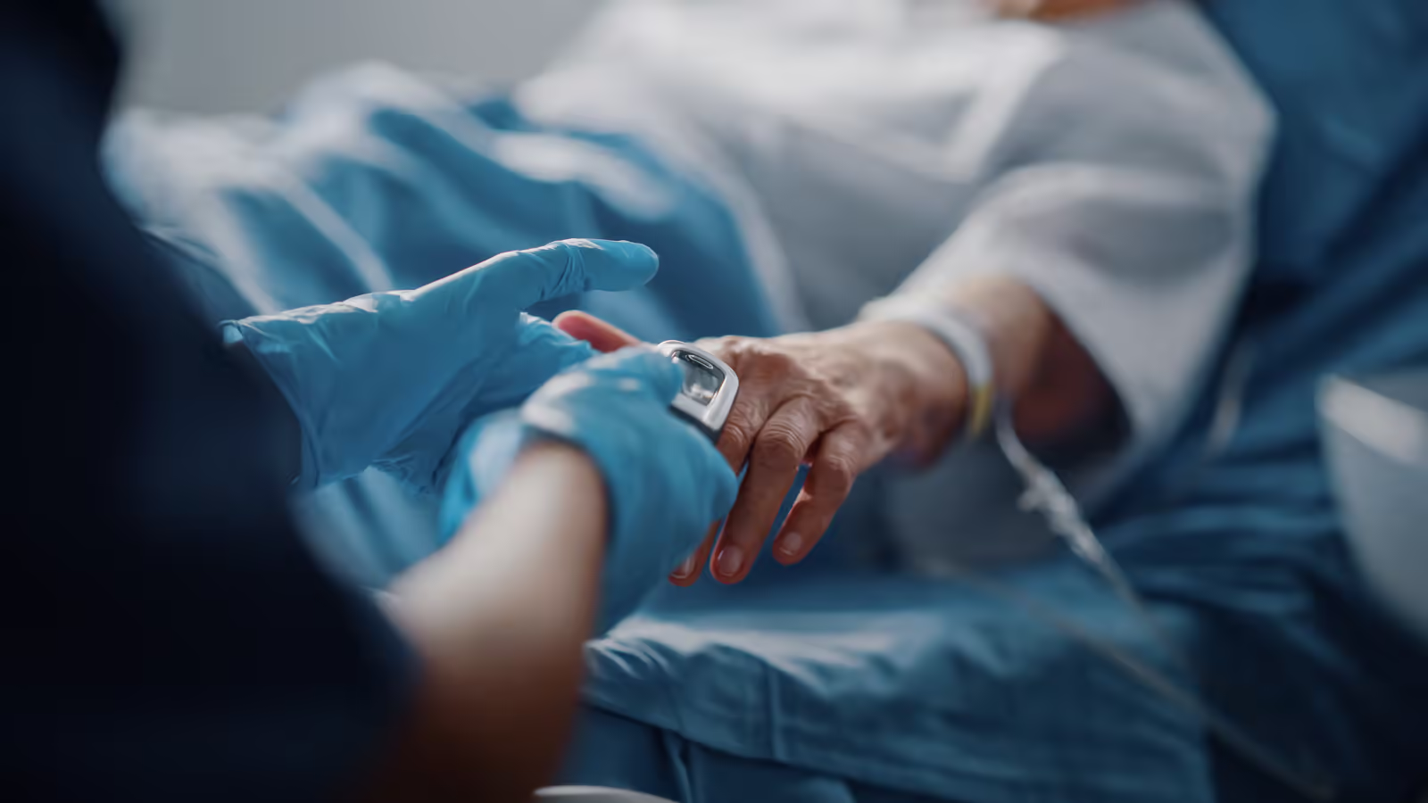Healthcare worker checking a patient's wrist monitor in a hospital bed