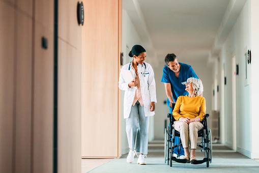 Doctor and nurse assisting an elderly patient in a wheelchair through a hospital corridor
